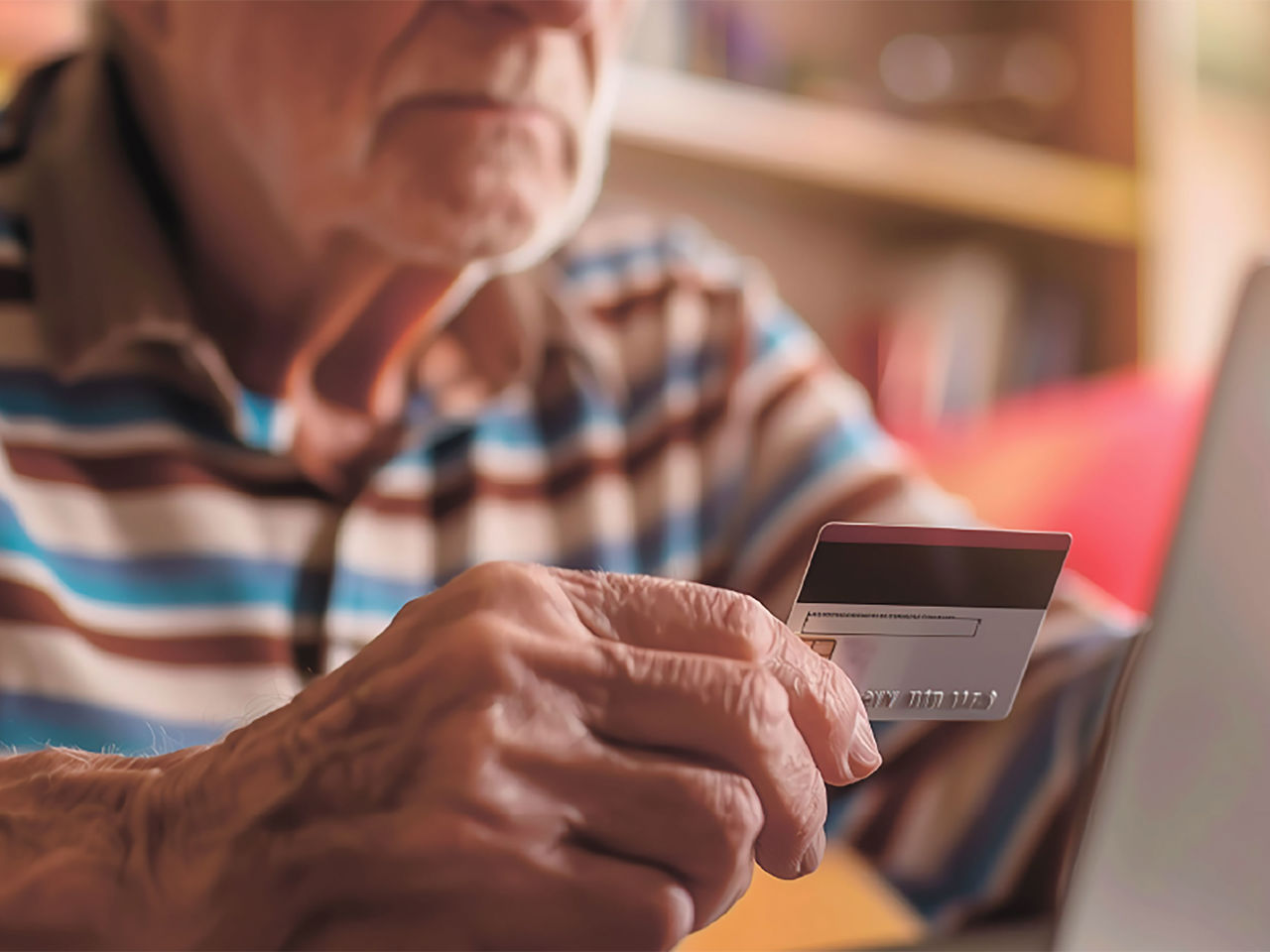 Ældre mand der holder et dankort op foran en PC