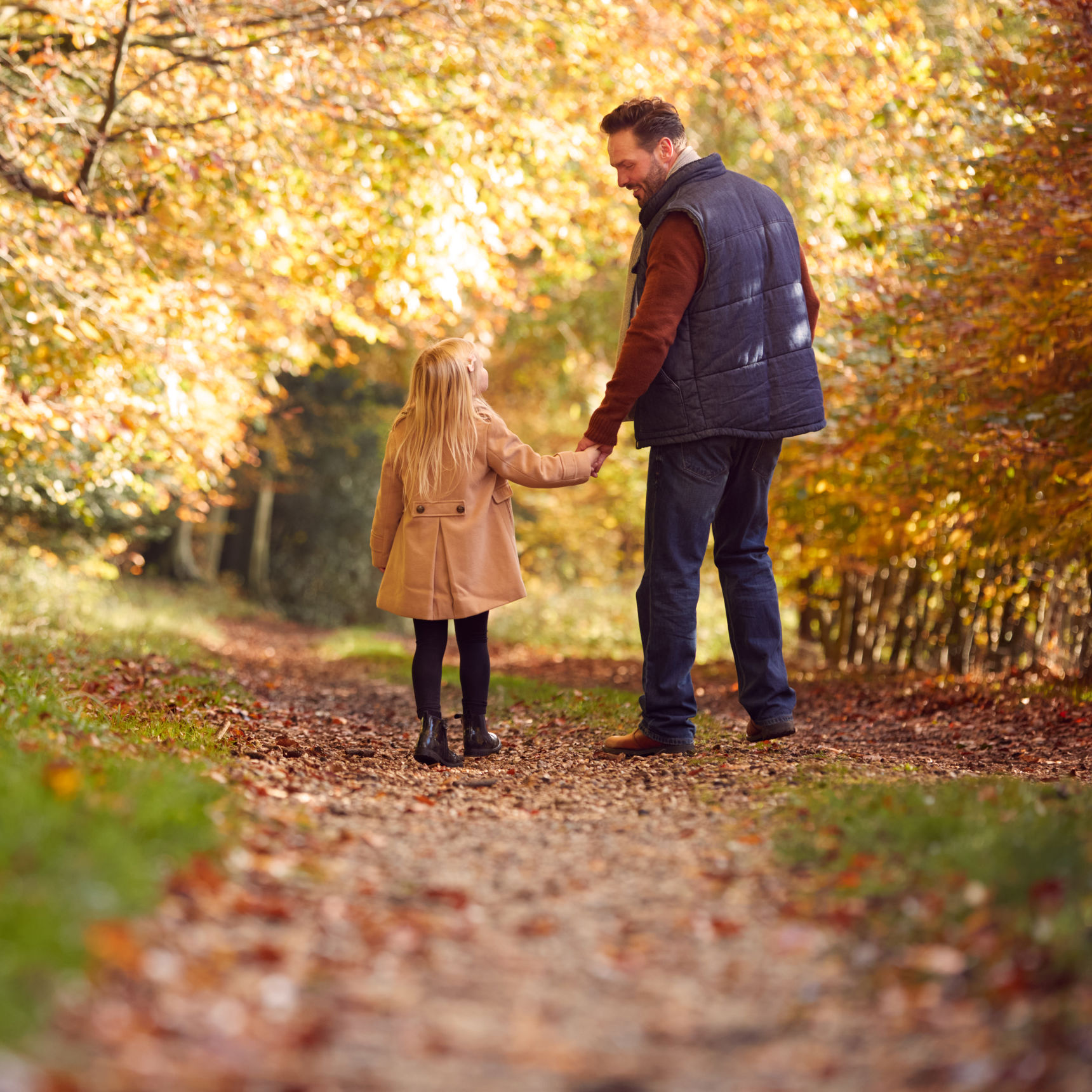 Mand holder barn i hånden i en efterårsskov