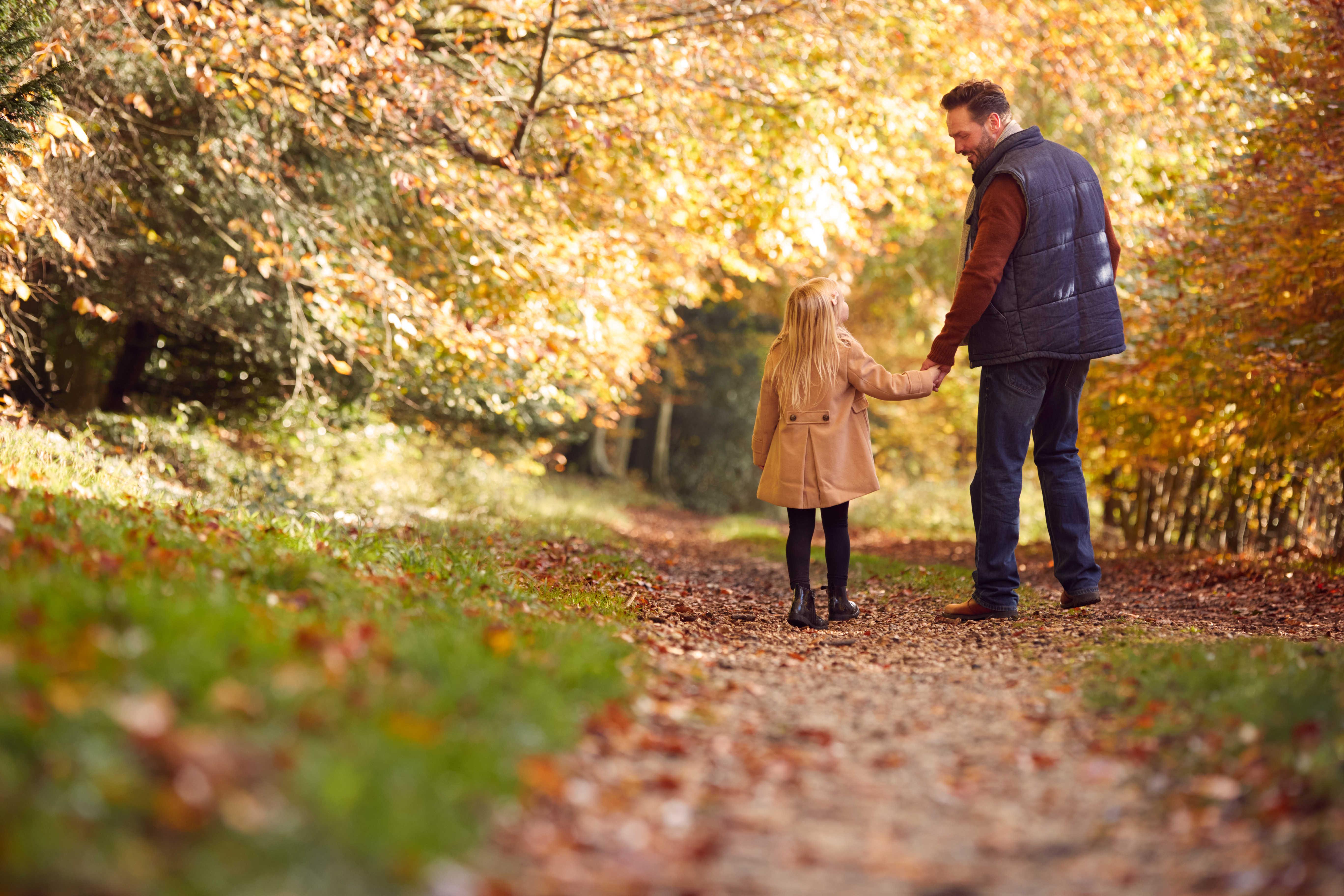 Mand holder barn i hånden i en efterårsskov