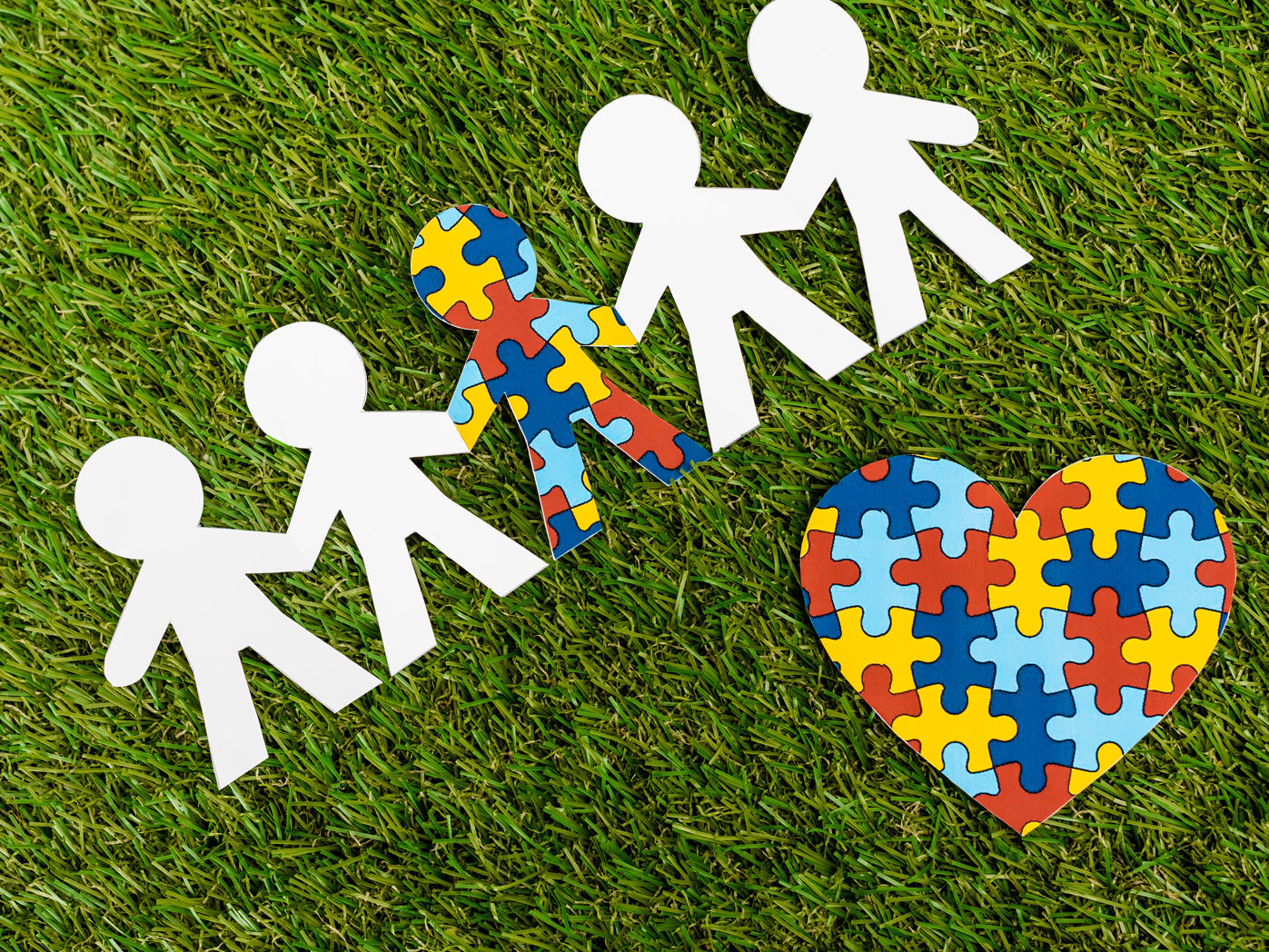 Hvide tændstikmænd på en græsplæne og en enkelt puslespilsbrik mand og et hjerte