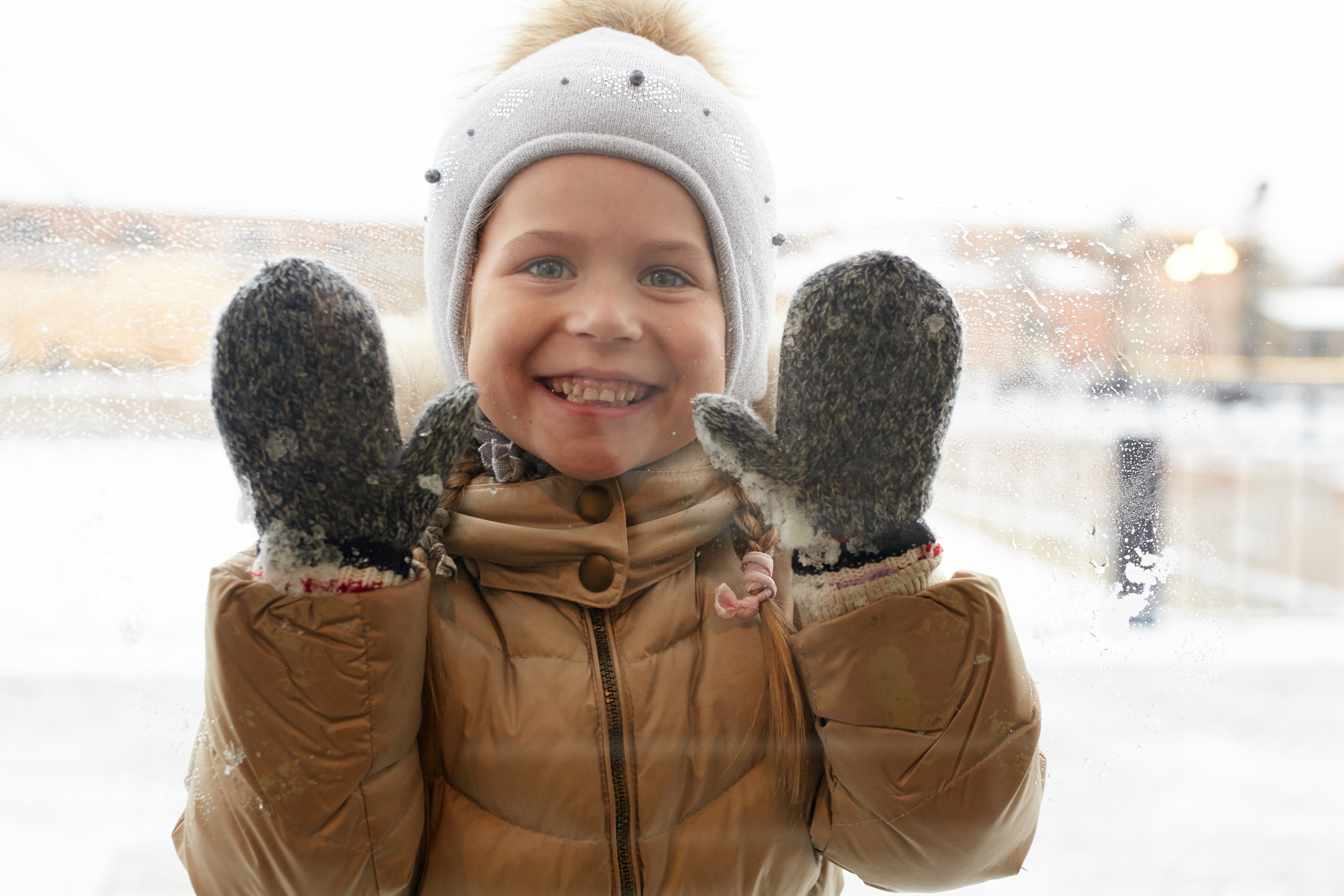 Barn med hue og handsker der kigger gennem en rude