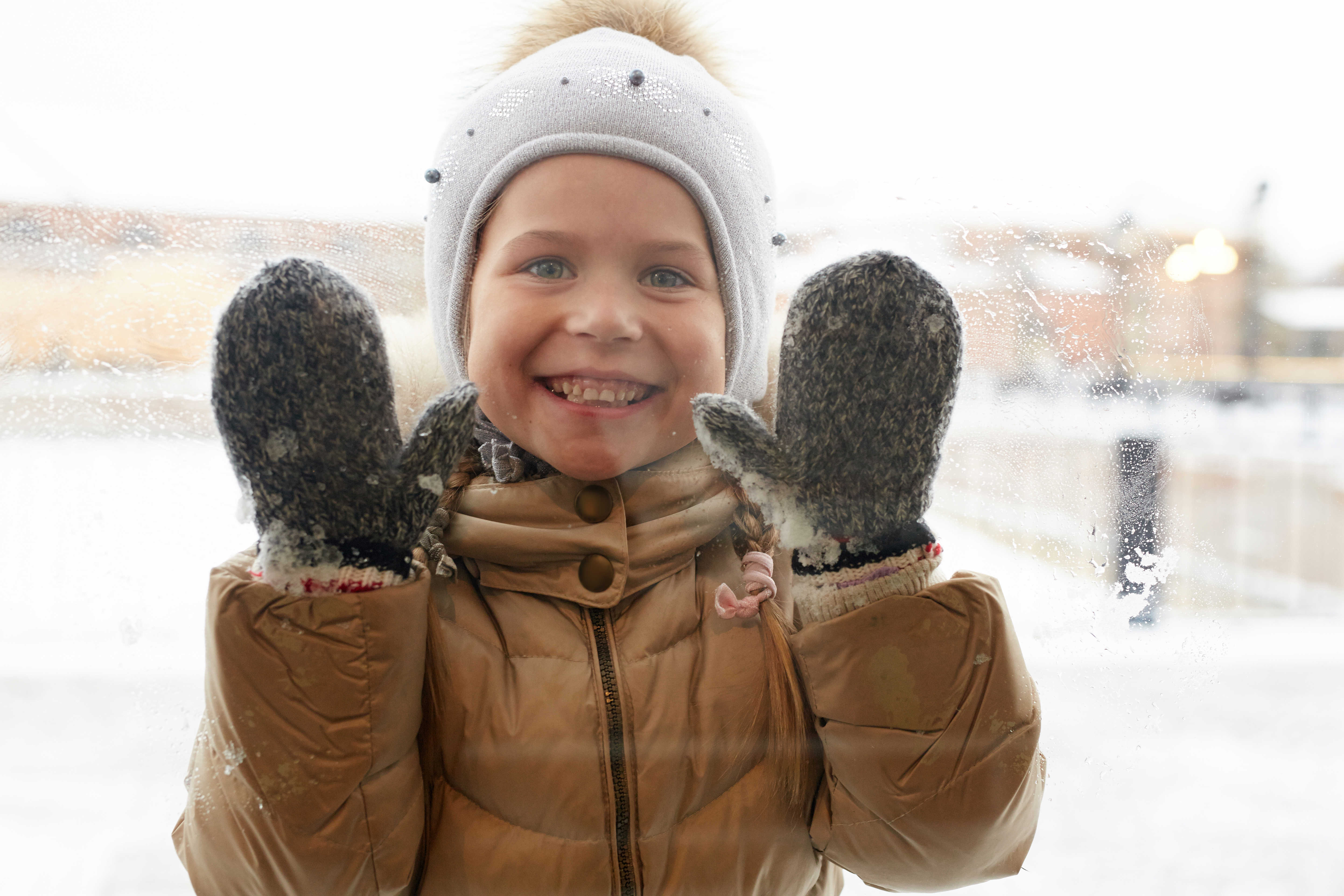 Barn med hue og handsker der kigger gennem en rude